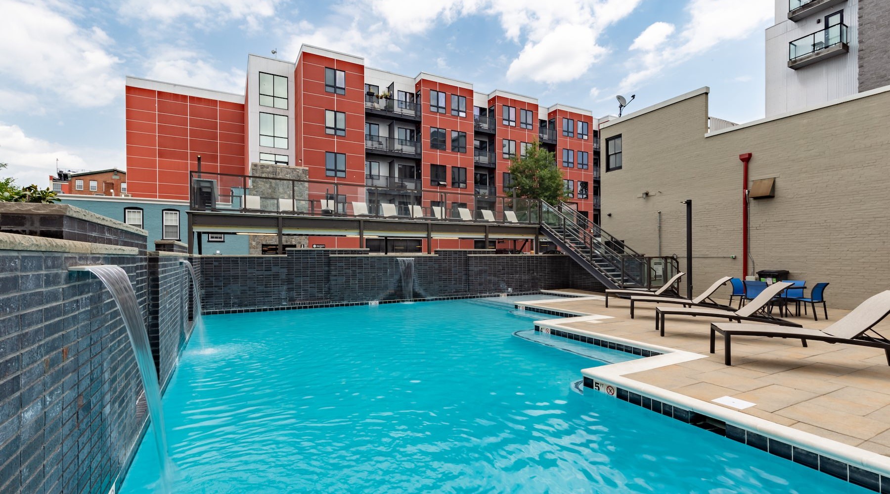 Relax and unwind poolside Resort-style swimming pool with lounge seating and building behind it